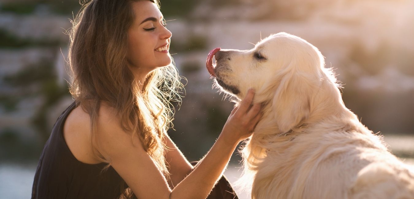 Woman petting a golden retriever dog outdoors with a blurred natural background